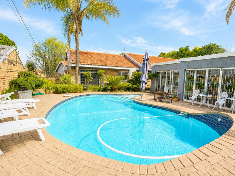 A well-maintained outdoor pool area featuring a paved deck, clear blue swimming pool, and direct access to the home through sliding glass doors.