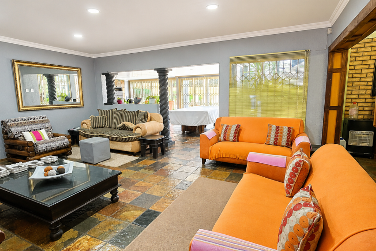 Spacious living area featuring natural slate tile flooring, recessed lighting, and decorative columns, opening into an adjacent space with exposed brick accents.