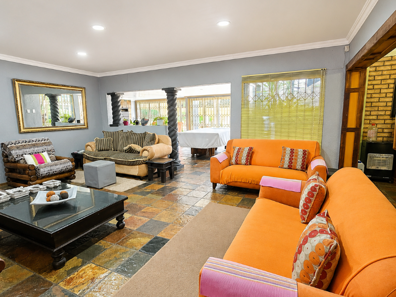 Spacious living area featuring natural slate tile flooring, recessed lighting, and decorative columns, opening into an adjacent space with exposed brick accents.