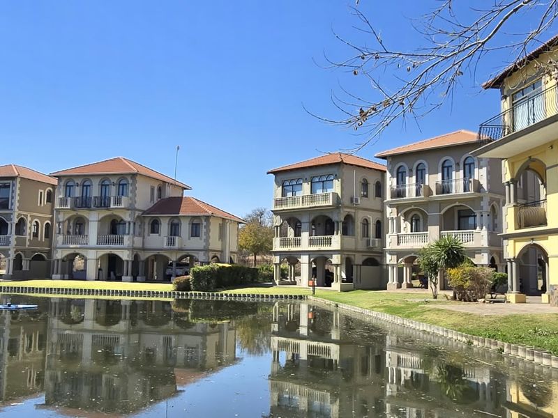 A scenic view of multi-story residential villas featuring Mediterranean-style architecture, arched balconies, and tiled roofs, situated directly along a waterfront.