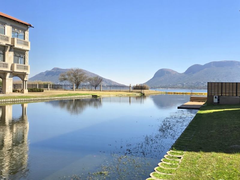 Scenic view of a canal-front property featuring a private jetty, manicured lawns, and mountain vistas in the background.