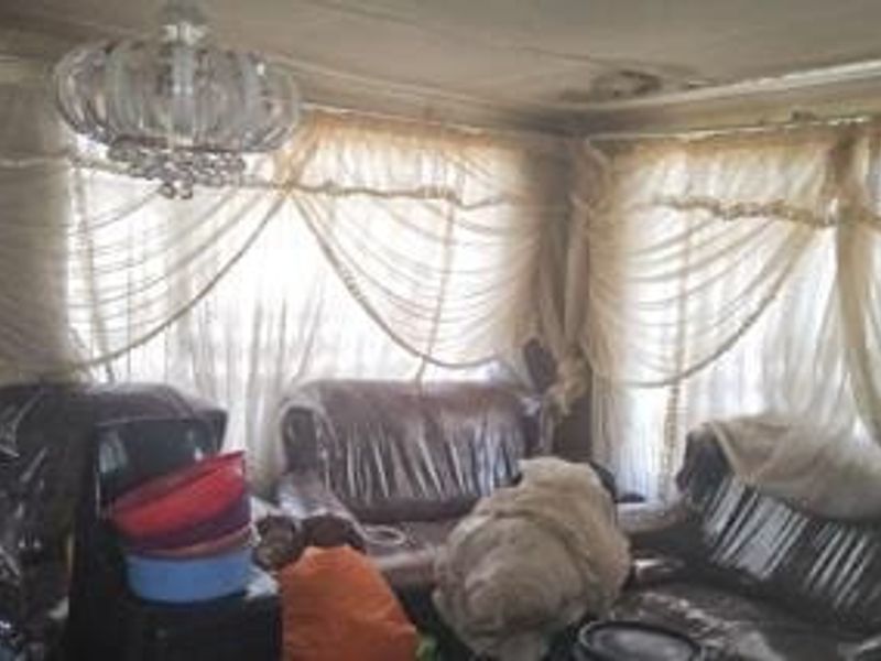 A living room space featuring a crystal chandelier and ceiling molding, currently showing significant signs of ceiling water damage and wear.