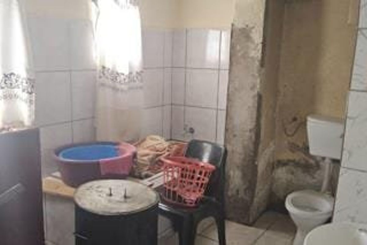 A small bathroom featuring a toilet and tiled wall finishes, currently requiring significant maintenance and cosmetic renovation to improve its overall condition.