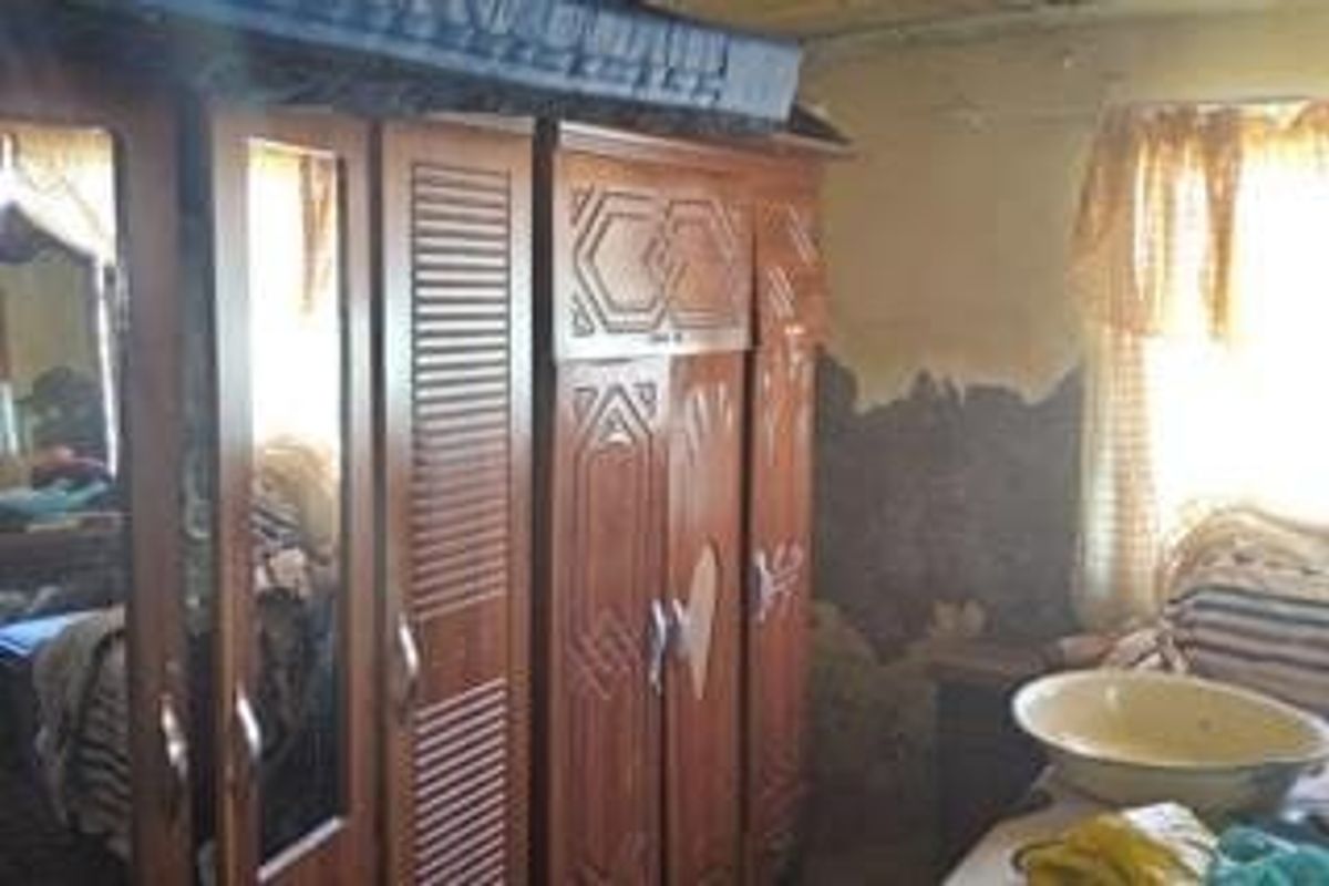 A bedroom featuring a large built-in wooden wardrobe, showing significant signs of wall surface damage and deterioration requiring repair and renovation.