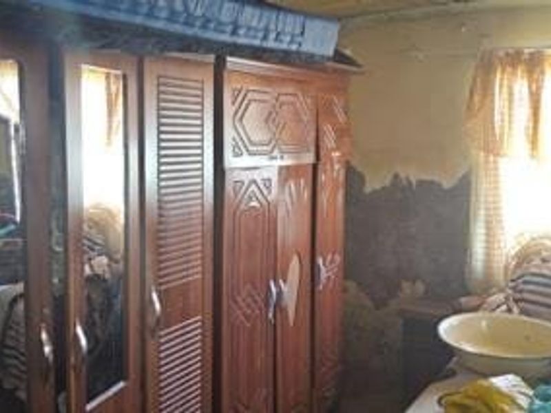 A bedroom featuring a large built-in wooden wardrobe, showing significant signs of wall surface damage and deterioration requiring repair and renovation.