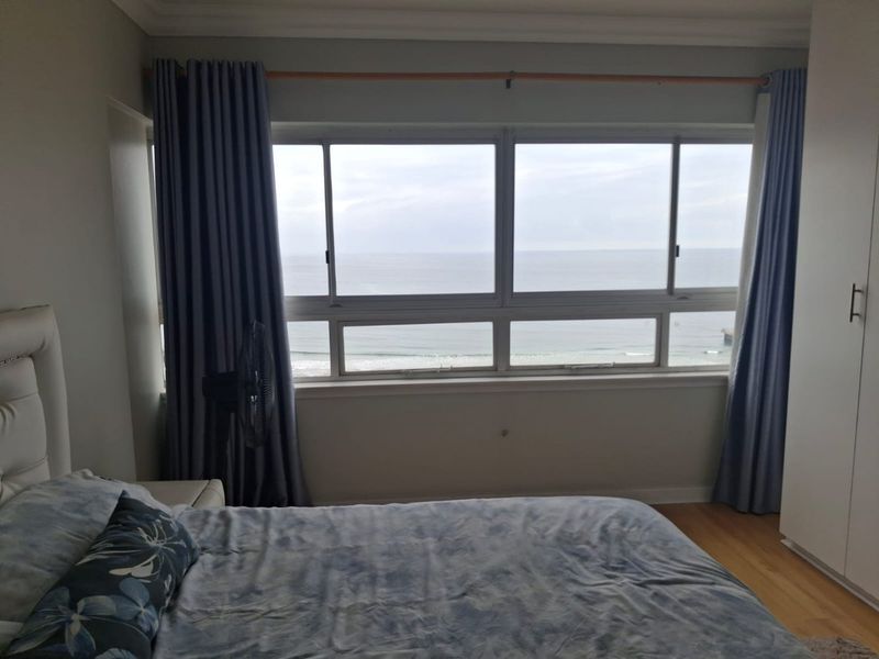 A well-lit bedroom featuring timber flooring, built-in wardrobes, and a large sliding window offering direct ocean views.