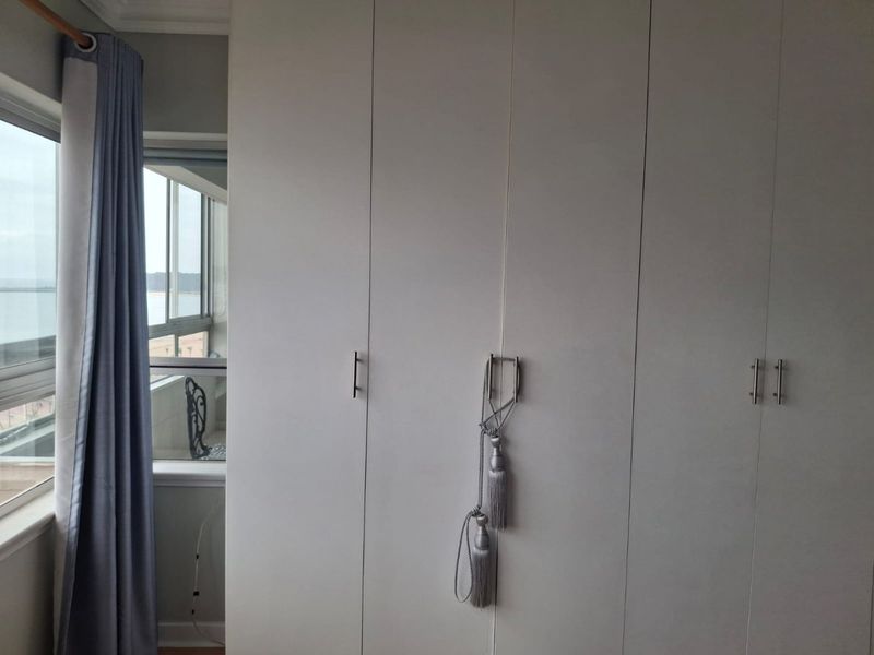 A bedroom featuring floor-to-ceiling built-in cupboards and a window with views of the exterior balcony.