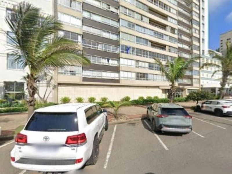 Exterior view of a multi-story apartment building featuring a paved parking area and landscaped surroundings.
