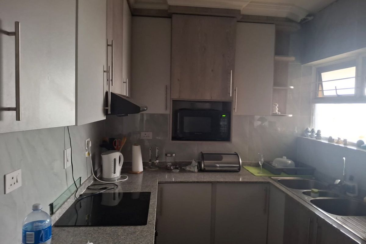 A functional kitchen featuring modern built-in cabinetry, granite countertops, a stainless steel double sink, and integrated appliances including a hob and microwave.