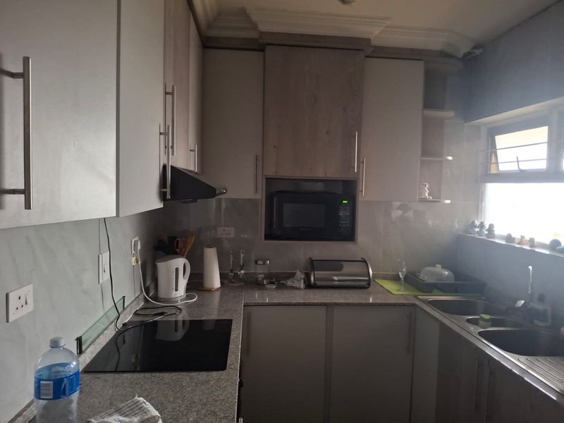 A functional kitchen featuring modern built-in cabinetry, granite countertops, a stainless steel double sink, and integrated appliances including a hob and microwave.