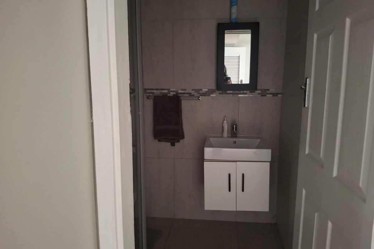 A compact bathroom featuring a wall-mounted vanity with basin, tiled walls with decorative mosaic accents, and a shower enclosure.