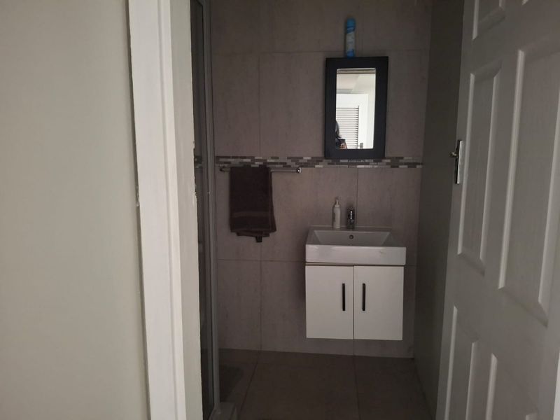 A compact bathroom featuring a wall-mounted vanity with basin, tiled walls with decorative mosaic accents, and a shower enclosure.