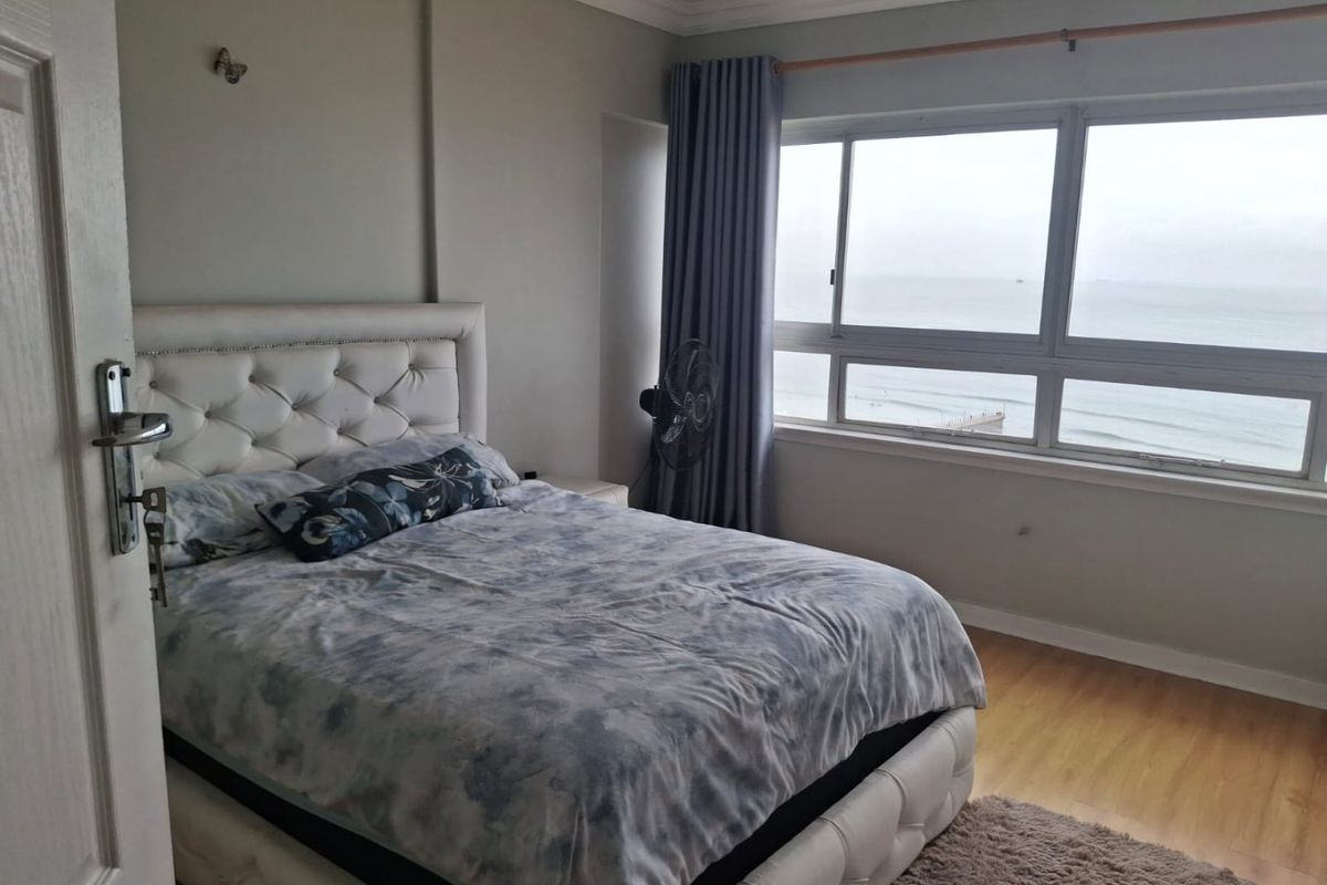 A well-lit bedroom featuring laminate flooring and a large window offering expansive ocean views.