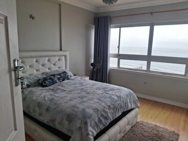 A well-lit bedroom featuring laminate flooring and a large window offering expansive ocean views.