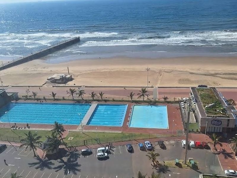 Elevated coastal view overlooking the public swimming pools, beach, and ocean horizon.