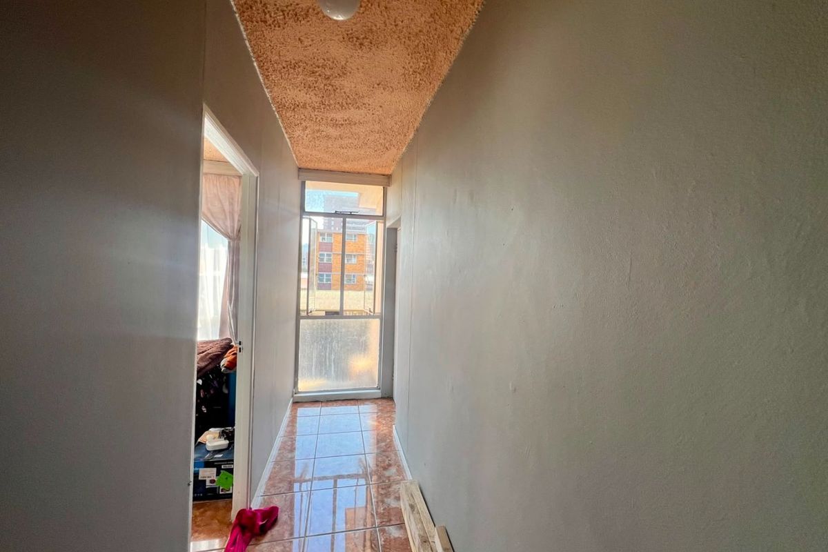 A narrow hallway featuring tiled flooring and a textured ceiling, leading towards a window that provides natural light.