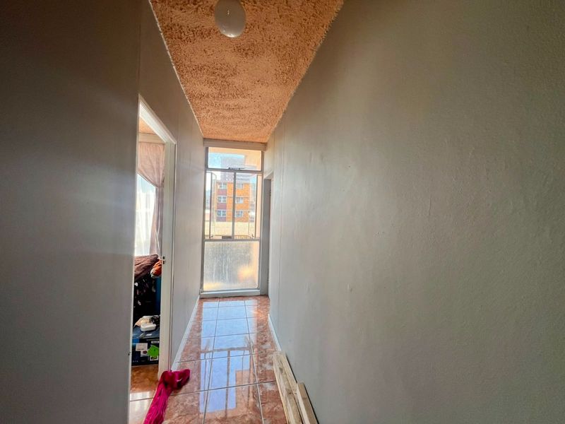 A narrow hallway featuring tiled flooring and a textured ceiling, leading towards a window that provides natural light.