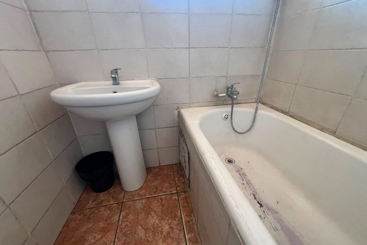 A compact bathroom featuring a pedestal basin and a bathtub with a wall-mounted shower mixer, finished with ceramic wall and floor tiles.