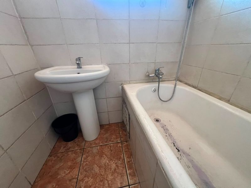 A compact bathroom featuring a pedestal basin and a bathtub with a wall-mounted shower mixer, finished with ceramic wall and floor tiles.