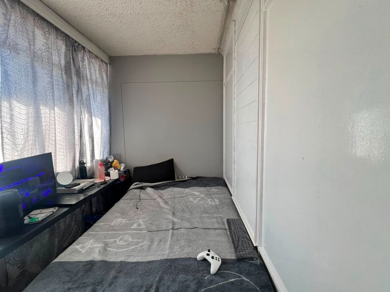 Compact bedroom featuring a built-in wardrobe and textured ceiling, offering a functional space that would benefit from cosmetic updates.