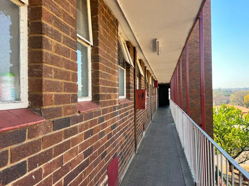 An exterior apartment building walkway featuring exposed brick walls, tiled flooring, and a metal safety balustrade overlooking the surrounding area.
