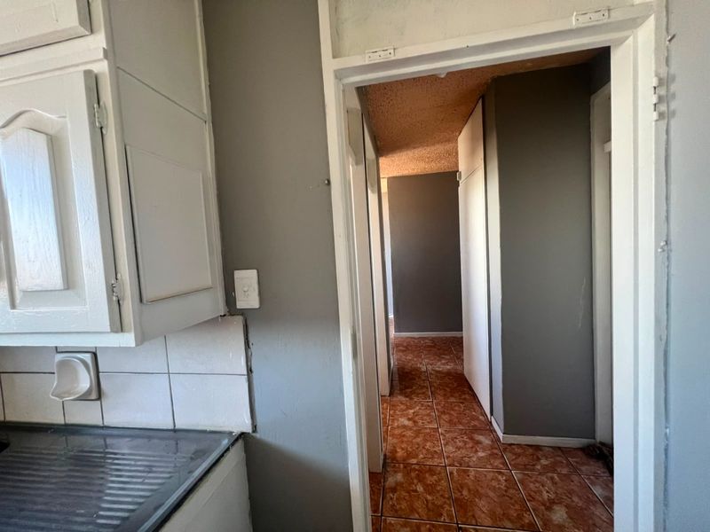 A view from the kitchen into a tiled hallway featuring textured ceilings and built-in storage, showing signs of wear and dated finishes.