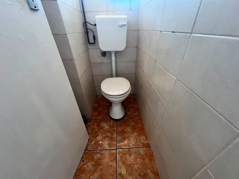 A small, functional bathroom featuring a standard toilet, tiled walls, and tiled flooring, currently in need of cosmetic updates.