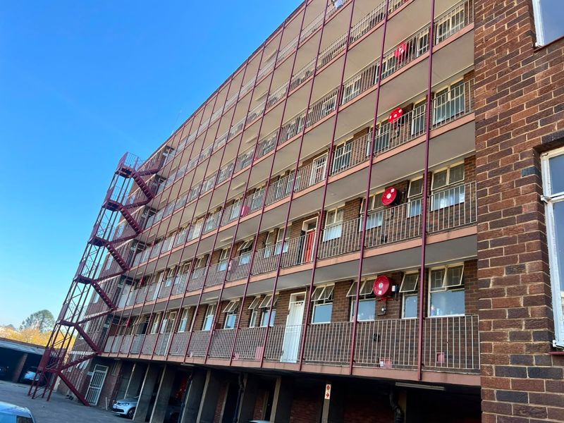 A multi-story apartment building facade featuring brick construction, external metal fire escape stairs, and balcony access for each level.
