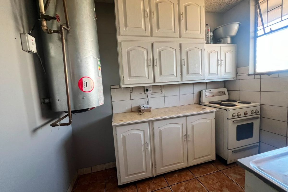 A functional kitchen featuring built-in cabinetry, an electric stove, tiled backsplash, and an exposed water heater, offering potential for modernization and cosmetic updates.