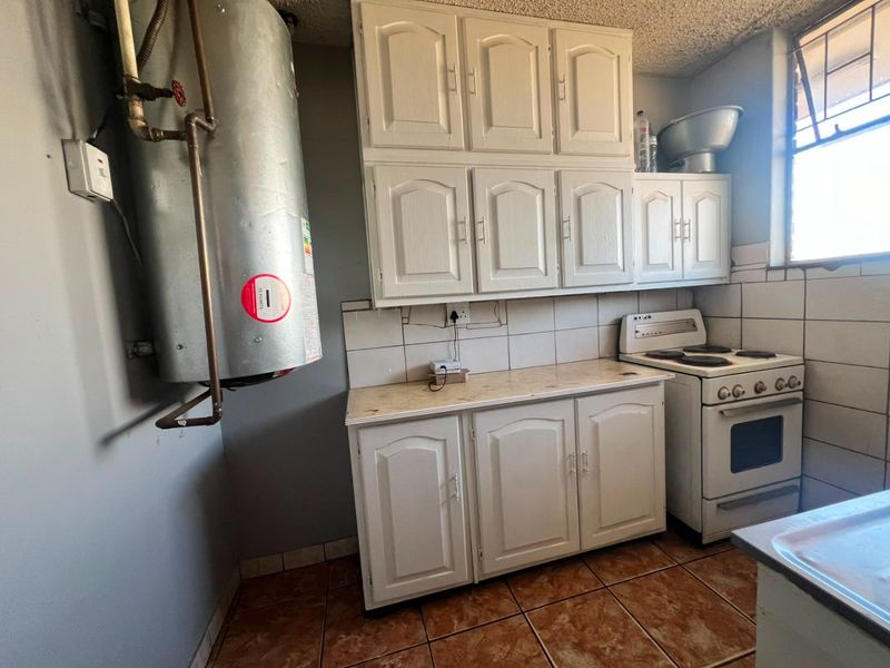 A functional kitchen featuring built-in cabinetry, an electric stove, tiled backsplash, and an exposed water heater, offering potential for modernization and cosmetic updates.