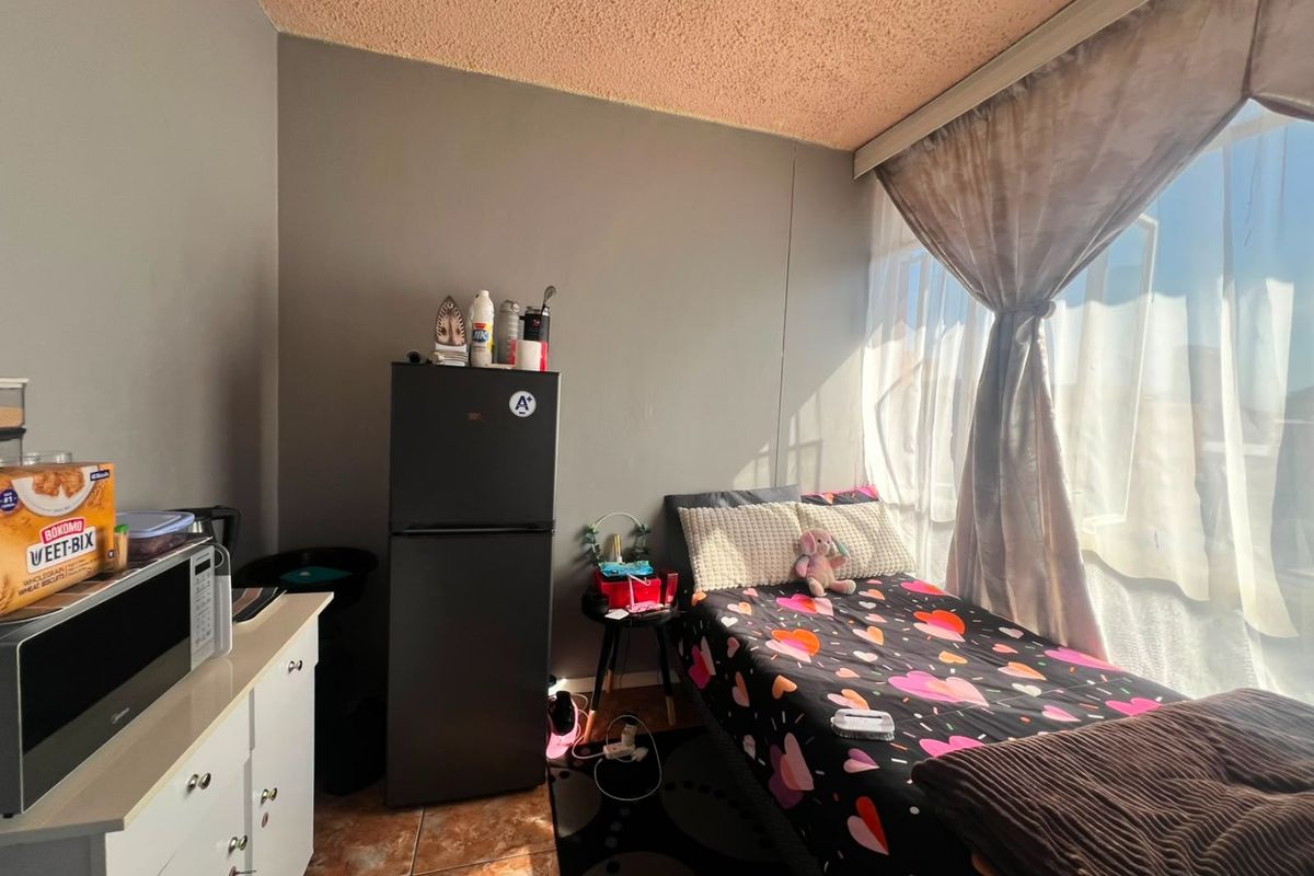 A compact bedroom featuring tiled flooring and a textured ceiling, with natural light provided by a large window.
