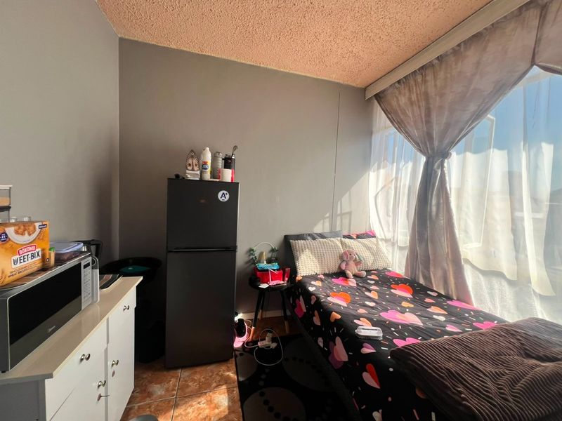 A compact bedroom featuring tiled flooring and a textured ceiling, with natural light provided by a large window.
