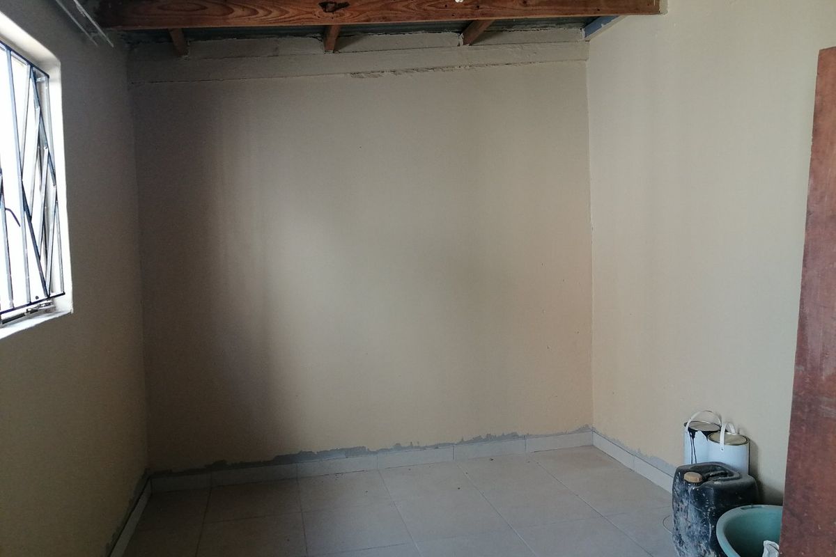 An empty bedroom featuring tiled flooring, exposed timber roof beams, and a corrugated metal ceiling, currently in an unfinished state.