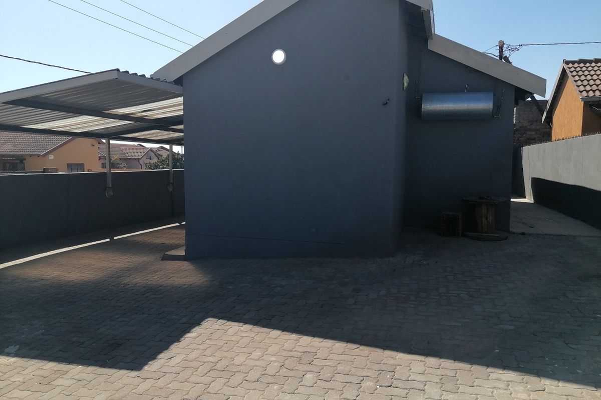 Rear exterior view of the property featuring a paved driveway, a covered carport structure, and a boundary wall.