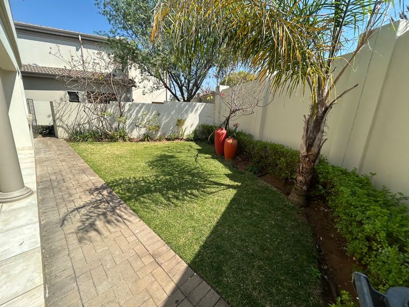 A well-maintained rear garden featuring a paved walkway, lush lawn, and perimeter boundary walls.