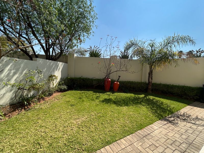 A well-maintained private garden featuring a manicured lawn, paved walkway, and high perimeter walls for added privacy.