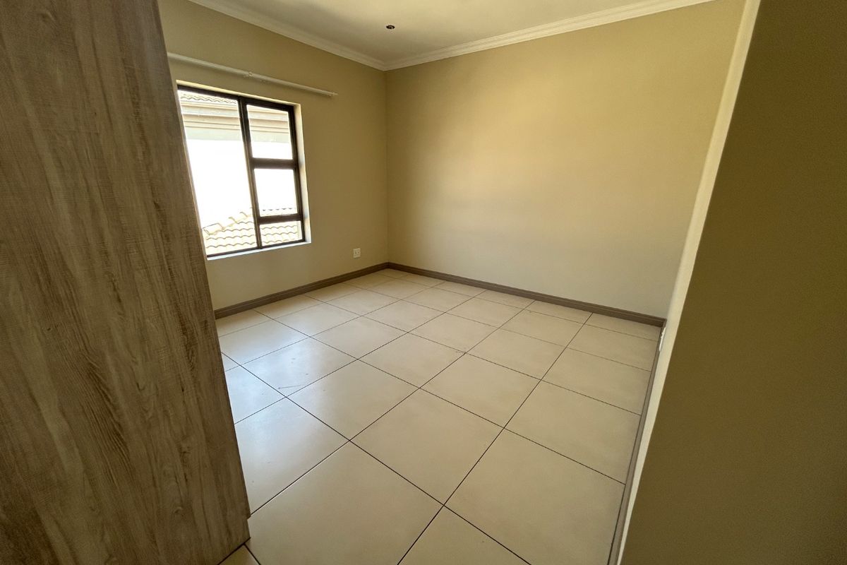 A clean, empty bedroom featuring neutral tiled flooring, built-in cupboards, and a large aluminium-framed window providing natural light.