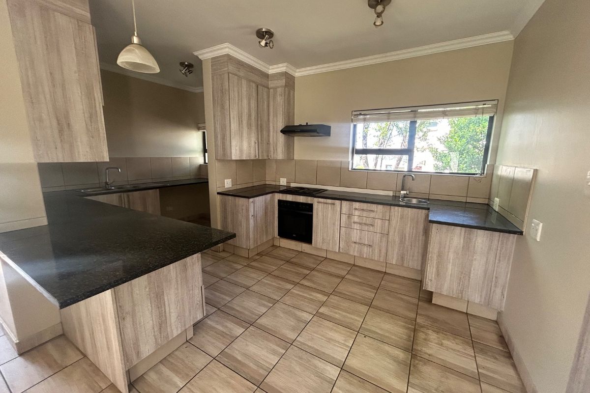 A spacious, modern kitchen featuring light wood-grain cabinetry, dark granite countertops, built-in oven and hob, and tiled flooring throughout.