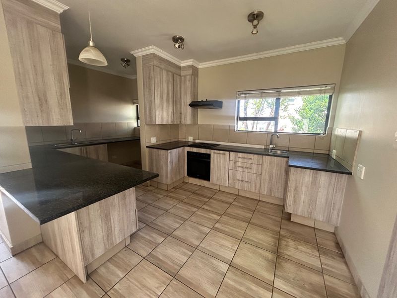 A spacious, modern kitchen featuring light wood-grain cabinetry, dark granite countertops, built-in oven and hob, and tiled flooring throughout.