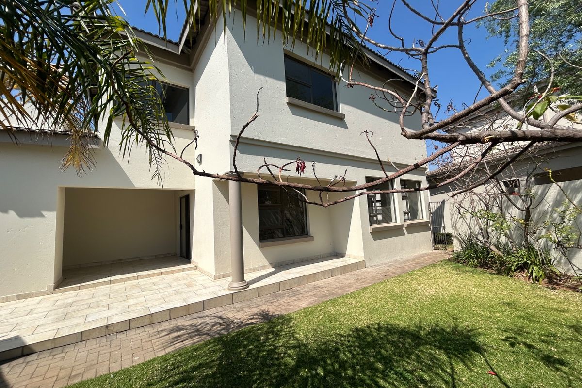 Rear view of the house featuring a covered tiled patio, paved walkway, and a well-maintained lawn area.