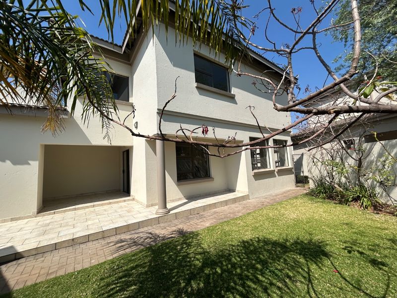 Rear view of the house featuring a covered tiled patio, paved walkway, and a well-maintained lawn area.