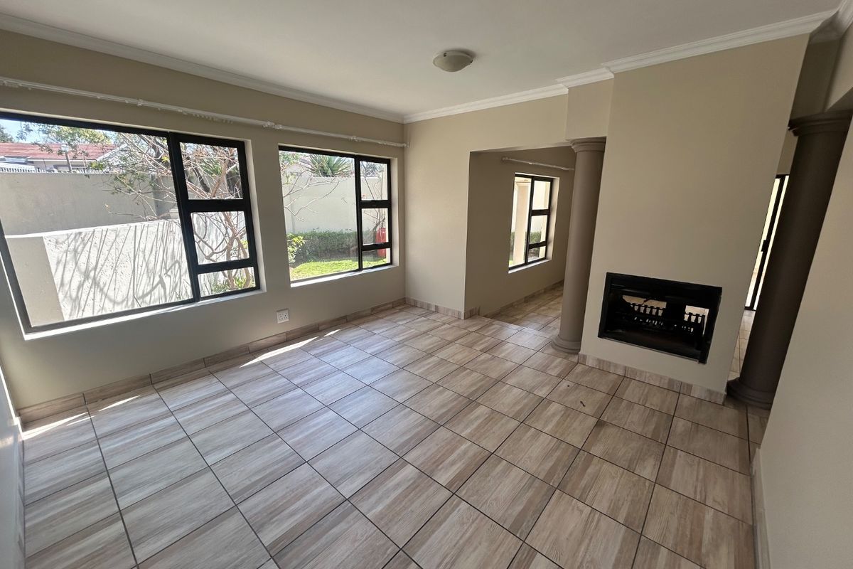Spacious, light-filled living area featuring neutral tiled flooring, a built-in fireplace, and large windows overlooking the garden.