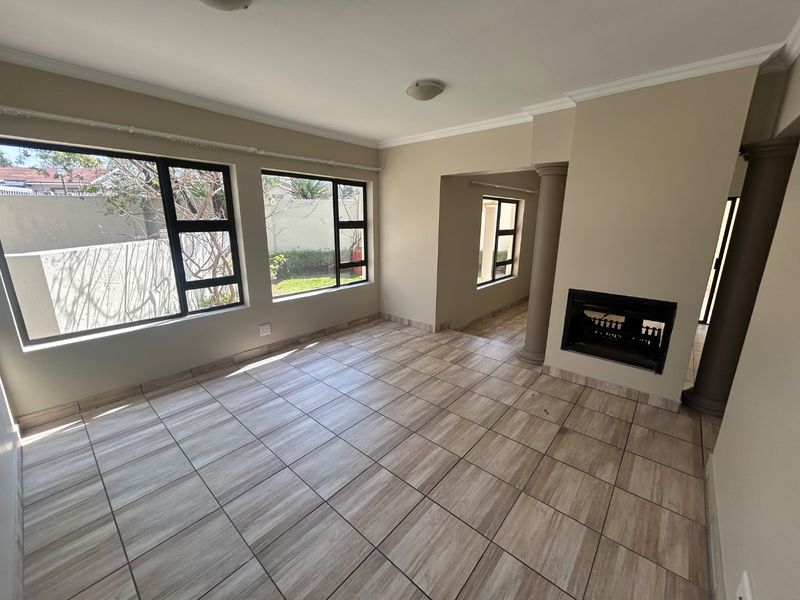 Spacious, light-filled living area featuring neutral tiled flooring, a built-in fireplace, and large windows overlooking the garden.