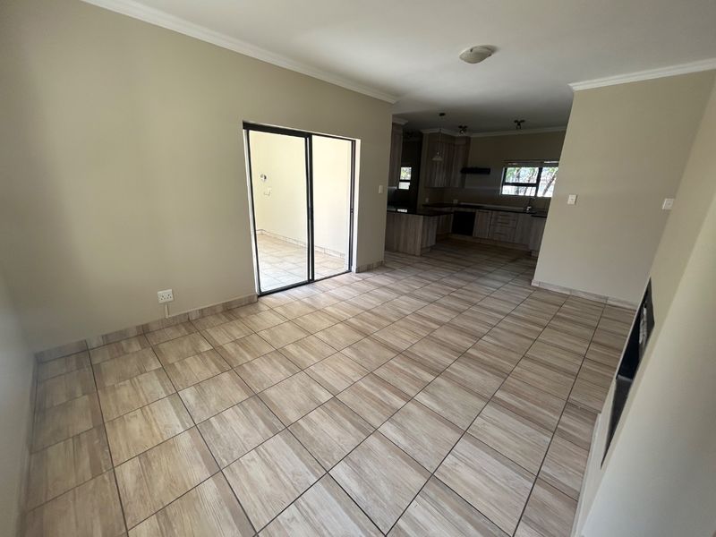An open-plan living and kitchen area featuring neutral tiled flooring, built-in cabinetry, and a sliding glass door leading to an outdoor space.