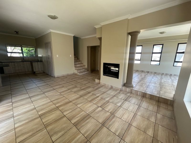 Spacious open-plan living area featuring tiled floors, a built-in fireplace, structural columns, and an integrated kitchen space with neutral finishes.