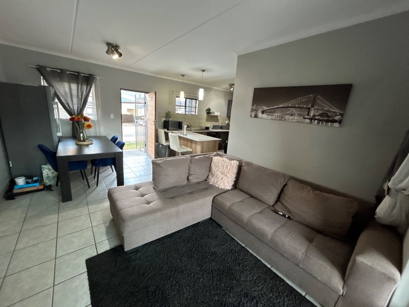 An open-plan living and dining area featuring tiled floors, a kitchen island, and direct access to the exterior through a security gate.