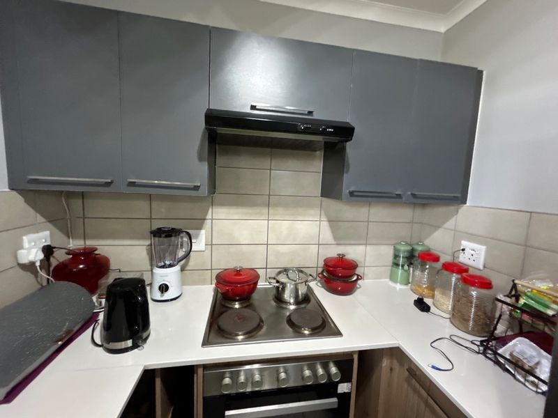 A functional kitchen featuring grey upper cabinetry, a tiled backsplash, stone countertops, and a built-in electric oven with a hob and extractor fan.