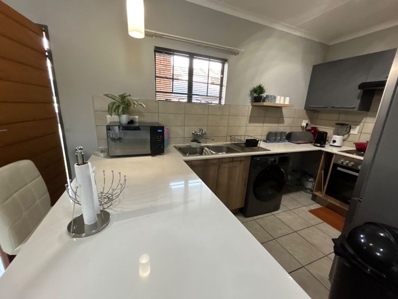 A functional kitchen featuring stone countertops, built-in cabinetry, a tiled backsplash, and integrated appliances including an oven and washing machine.
