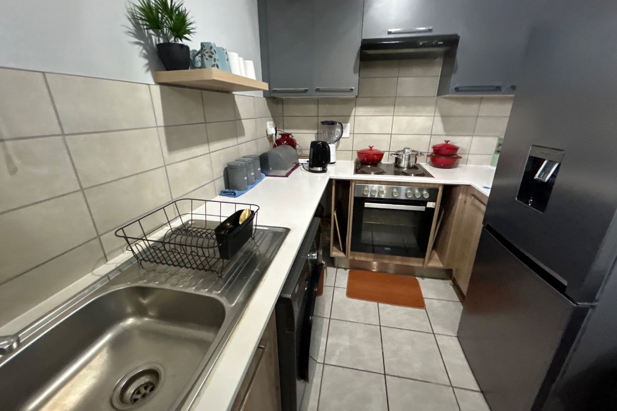 A functional kitchen featuring modern grey cabinetry, a stainless steel sink, built-in oven with cooktop, extractor fan, and neutral tiled finishes.