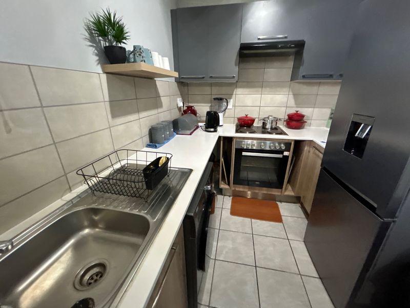 A functional kitchen featuring modern grey cabinetry, a stainless steel sink, built-in oven with cooktop, extractor fan, and neutral tiled finishes.
